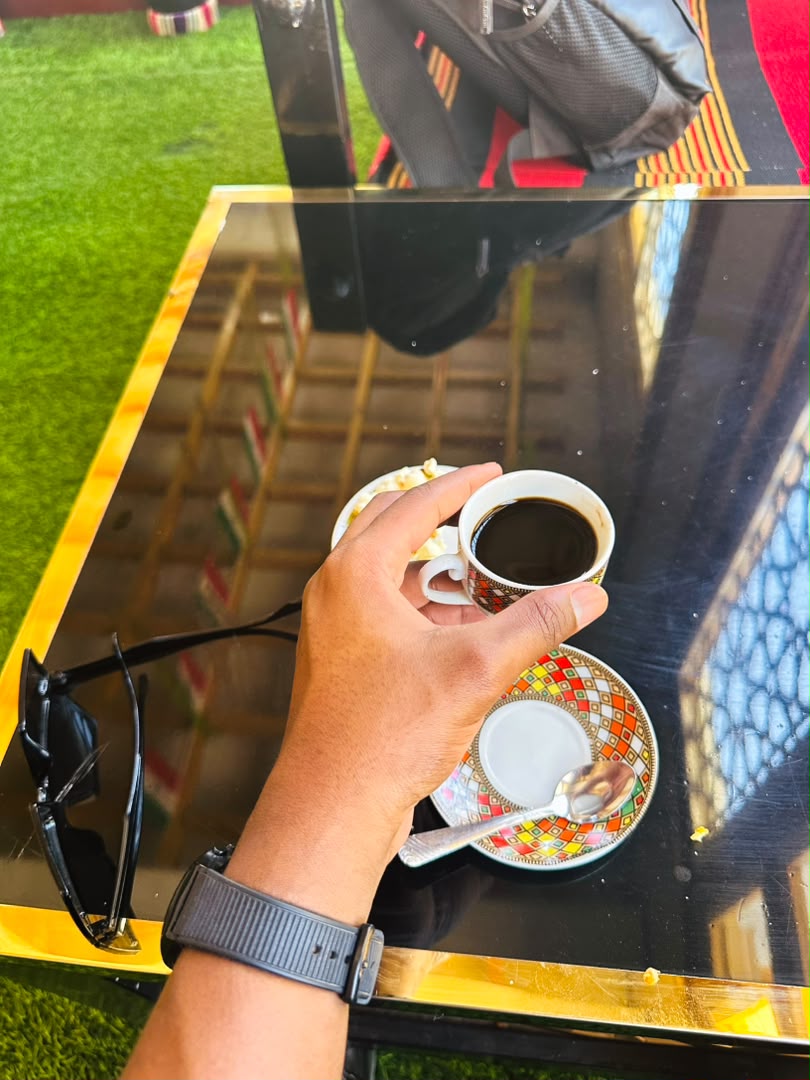 A hand holding a small cup of coffee above a colorful saucer